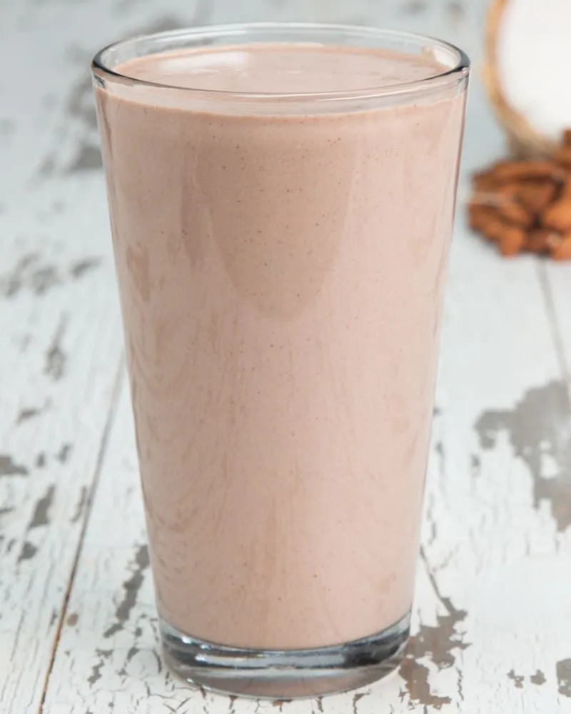 Pouring a thick homemade protein smoothie from a blender into a glass.